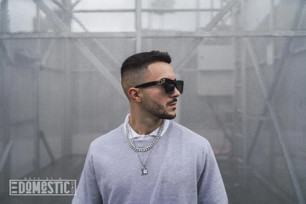 Stylish young attractive man wearing a sweater over a shirt with necklaces and sunglasses