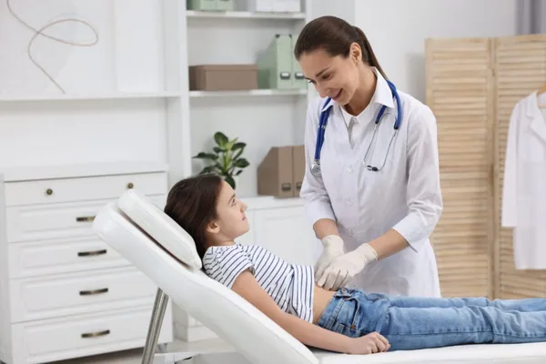 Gastroenterologist examining girl with stomach ache on couch in clinic