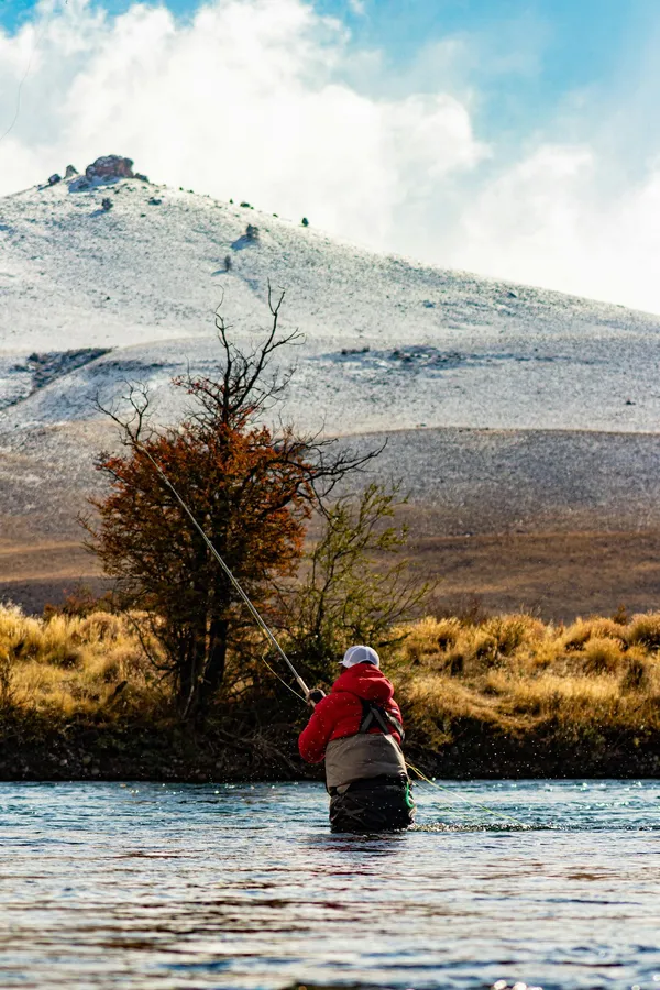 A fly fisherman stands in a pristine river set against the backdrop of Neuquén's autumnal landscape.