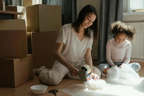 A mother and daughter packing boxes while preparing for a move in a sunlit room.
