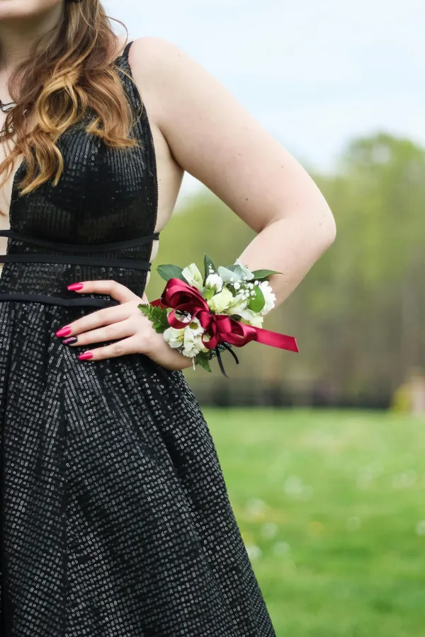 A woman's hand wearing a corsage on a black dress in an outdoor setting.