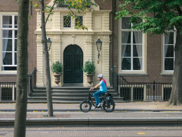 Adult cyclist wearing helmet rides through city street past historic building.