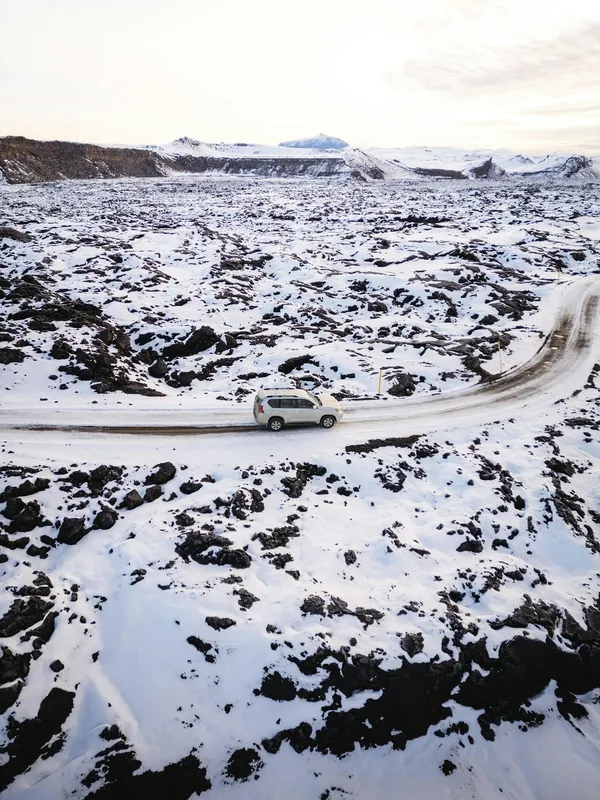 Aerial view of an SUV navigating a snowy Icelandic landscape, capturing winter's serene isolation.