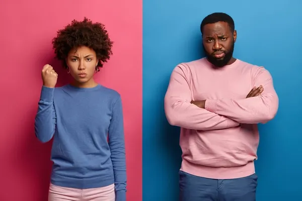 Angry dissatisfied woman clenches fist and shows her power, black unshaven man stands near with arms folded