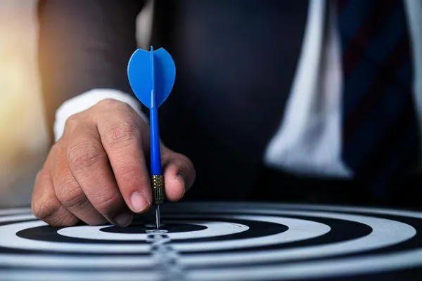 Close-up of a man's hand holding a blue dart on a bullseye, symbolizing precision and focus.