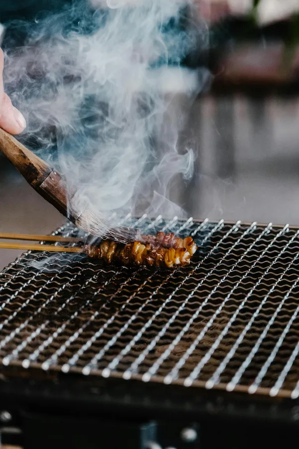 Close-up of juicy skewered meat grilling with smoke rising on a barbecue.
