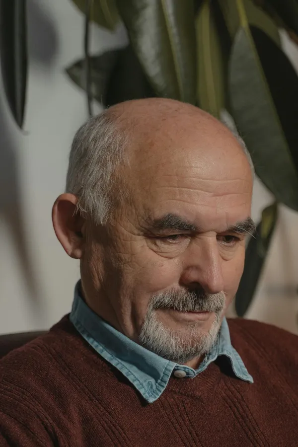 Close-up portrait of a thoughtful senior man with white hair and a goatee indoors.