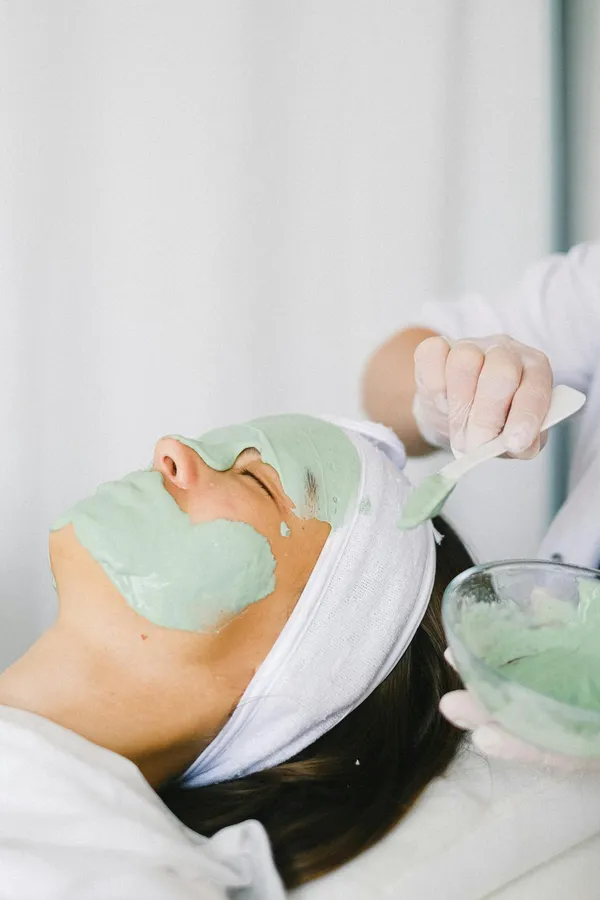 Cosmetician applying facial mask on client face