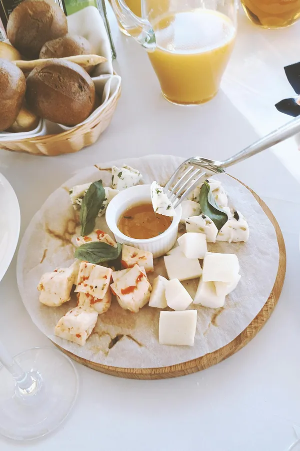 Elegant cheese platter with assorted cheeses, fresh basil, and a dipping sauce, complemented by fresh juice.