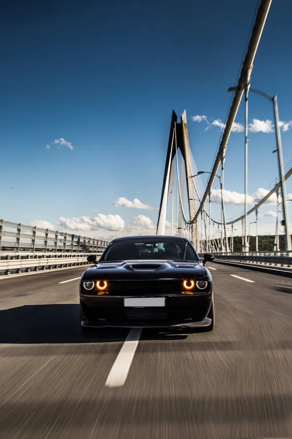 black muscle car driving over cable bridge