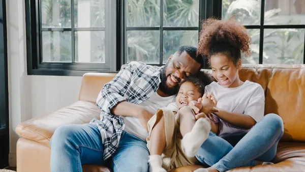 Happy cheerful african american family dad and daughter having fun cuddle play on sofa while birthday at house.