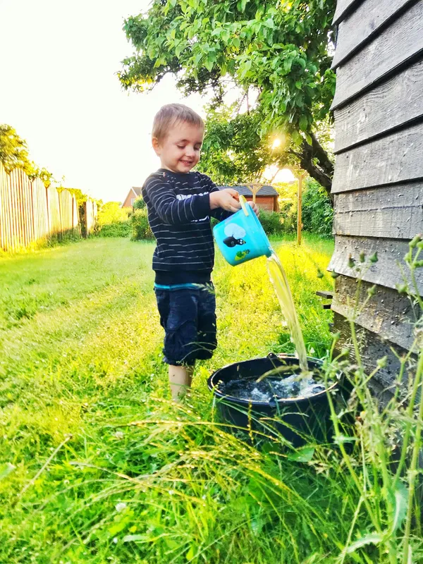Happy child playing in a sunny backyard with a watering can, enjoying a carefree summer day.