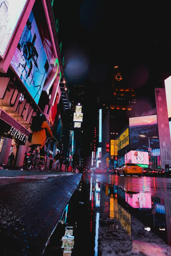Illuminated street scene of Times Square with neon lights and reflections at night in NYC.
