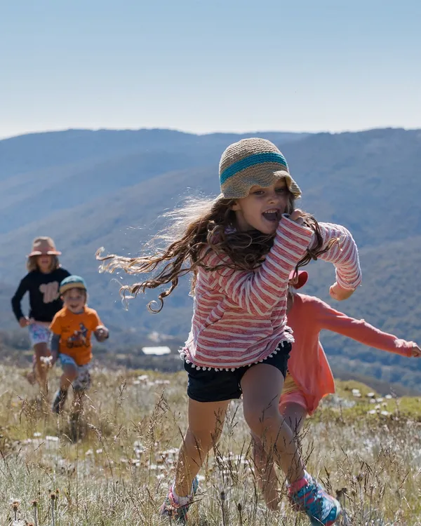 Kids running and playing in the alpine fields of Thredbo surrounded by mountains.
