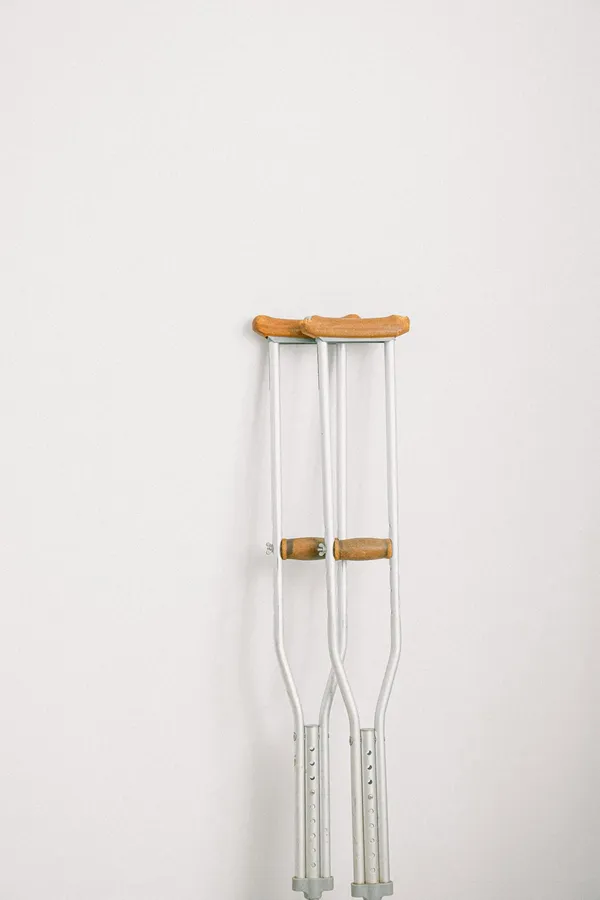 Minimalist image of crutches leaning on a white wall indoors.