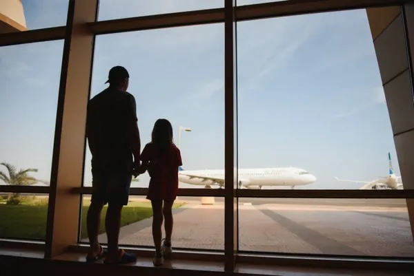Father and daughter looking out an airport window,