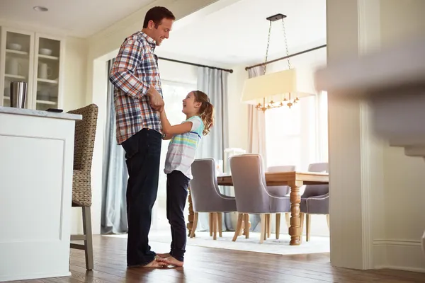 Father and young daughter smiling together in a bright kitchen, representing a safe and secure home environment for kids.