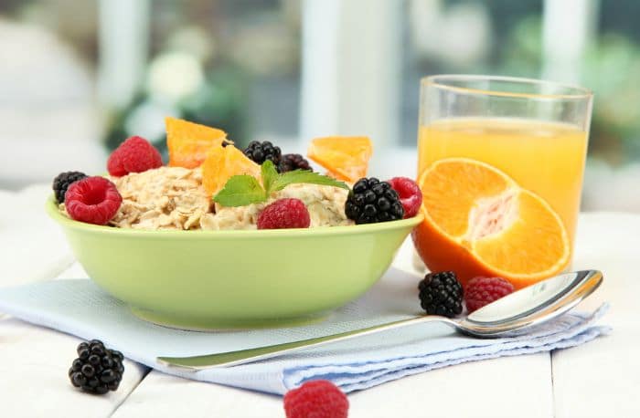 tasty oatmeal with berries and glass of juice on table, on window background