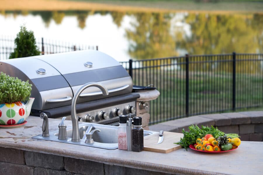 bbq area - Preparing a healthy summer meal in an outdoor kitchen with gas barbecue and sink on a brick patio overlooking a tranquil lake with tree reflections