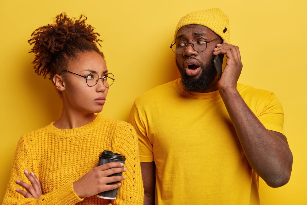 Upset jealous afro wife looks at husband who talks on mobile phone