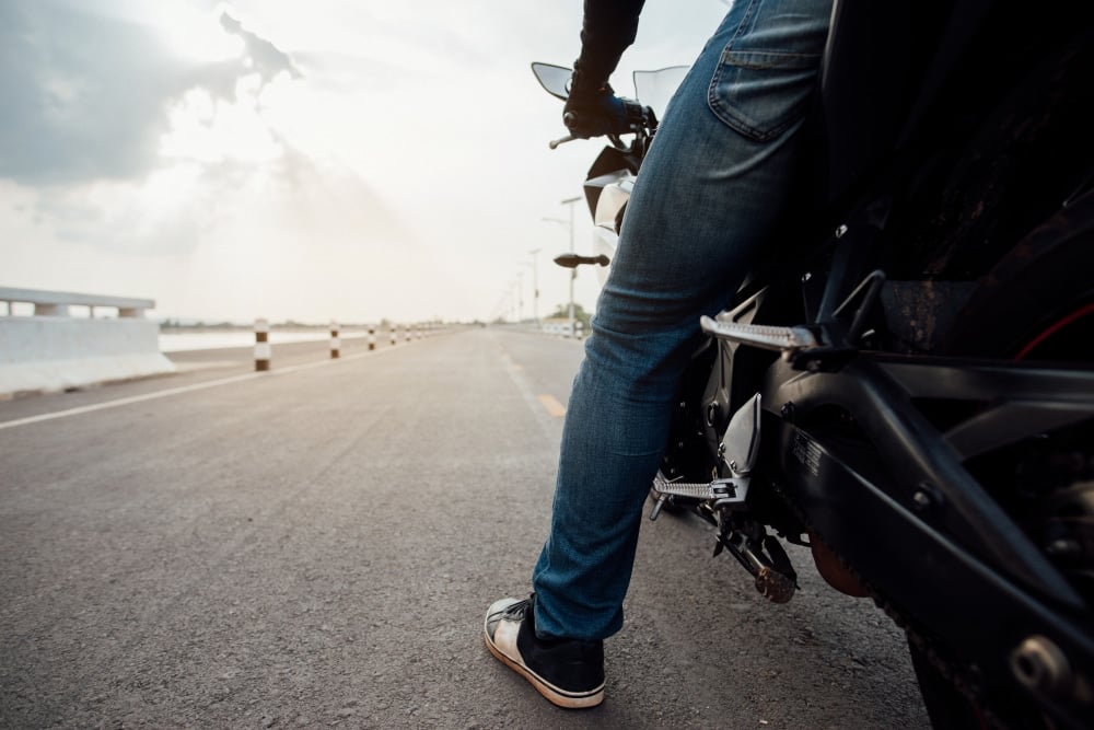 Male sitting on a motorbike looking down a empty road