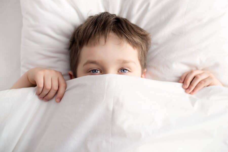 little boy in bed covering his face with white blanket