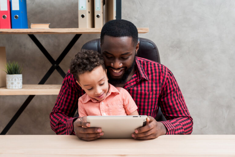 Black father and son using tablet at table