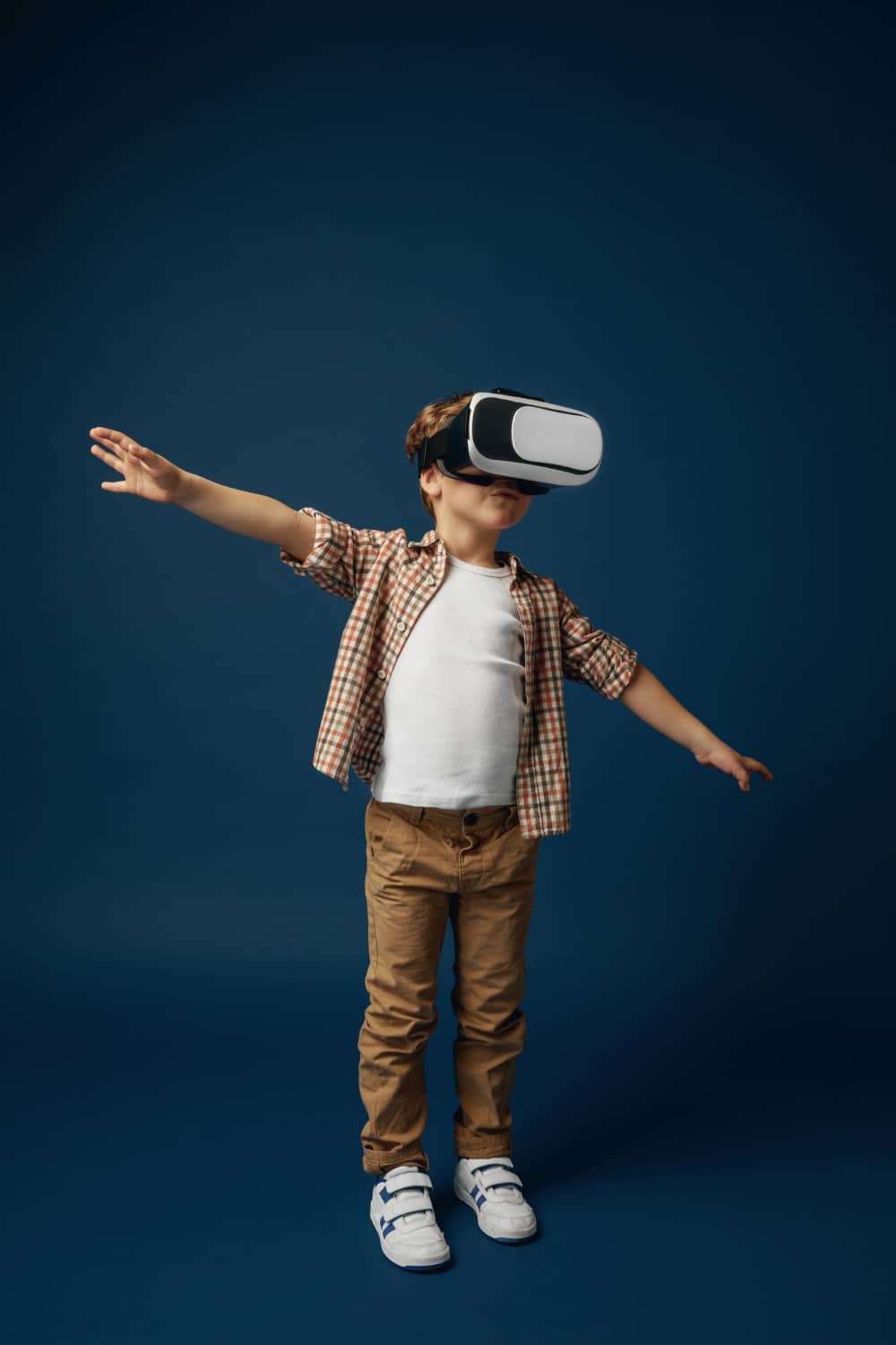 Weightless in the sky. little boy or child in jeans and shirt with virtual reality headset glasses isolated on blue studio background. concept of cutting edge technology, video games, innovation.