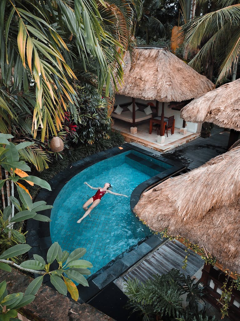 A woman enjoying leisure time floating in a tropical resort pool surrounded by lush greenery.