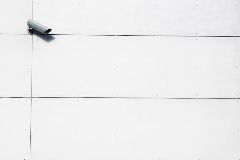 A minimalist image showcasing a single surveillance camera mounted on a stark white wall.