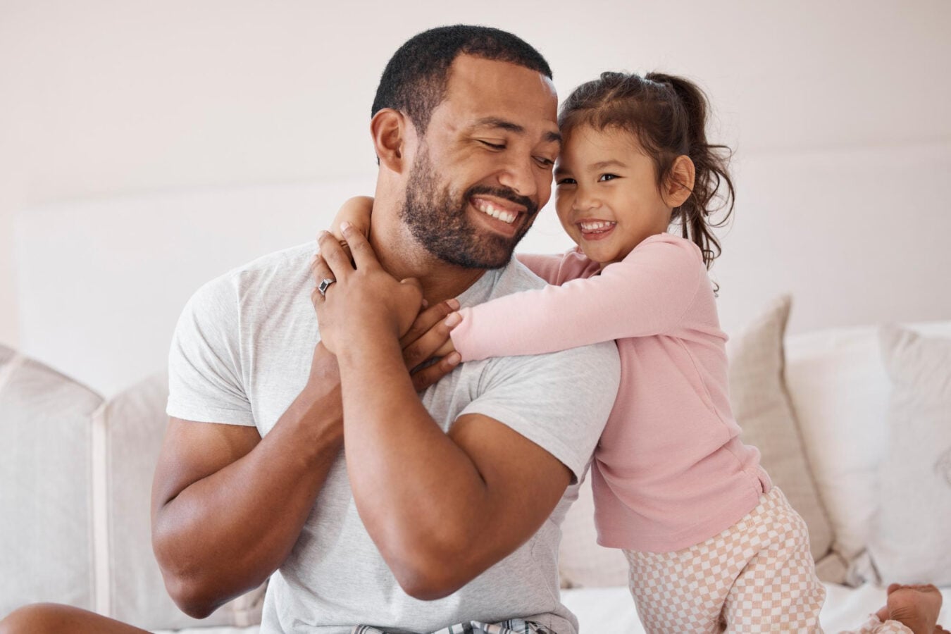 Smiling daughter hugs her dad on the bed; warm father–daughter bond, pure “Girl Dad” energy.